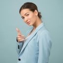 A young woman in a blue suit exhibits confidence with a relaxed pose against a blue background.