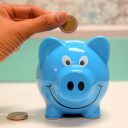 Hand inserting a coin into a blue piggy bank for savings and money management.